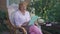 Portrait of positive Caucasian senior woman scrolling social media surfing Internet on tablet sitting on porch outdoors