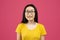 Portrait of positive chinese woman wearing glasses and looking to camera, posing over pink studio background