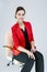Portrait of Positive Confident Female Enterpreneur Posing in Red Blazer in Chair Against White