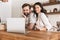 Portrait of positive couple looking at laptop while cooking pastry in kitchen at home