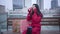 Portrait of positive cute Caucasian woman in red coat sitting on bench in the city with shopping bags and talking on the