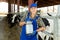 Portrait of positive dairy farm worker in blue overalls with can of milk on background of cows in stall