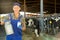 Portrait of positive dairy farm worker in blue overalls with can of milk on background of cows in stall