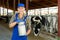 Portrait of positive dairy farm worker in blue overalls with can of milk on background of cows in stall
