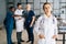 Portrait of positive female doctor in white uniform standing in medical meeting office, holding hands in pockets