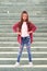 Portrait of a positive girl with long hair  standing on the steps of a high city staircase