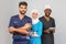 Portrait of positive healthcare workers standing in the hallway and looking at the camera. Group of paramedics smiling over gray