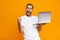 Portrait of positive man 30s in white t-shirt holding silver laptop, isolated over yellow background