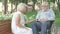 Portrait of positive paralyzed man in wheelchair talking with senior woman in sunny park. Relaxed carefree couple of