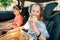 Portrait of positive smiling girl eating just cooked italian pizza sitting with a sister on car back seat in child car seats.