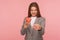 Portrait of positive woman employee in suit jacket holding sweet doughnut and pointing to camera, showing unhealthy snack