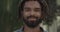 Portrait of positive young guy with dreadlocks looking to camera and smiling. Headshot of handsome mixed race bearded