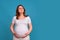 Portrait of a pregnant woman in perplexity on a blue background