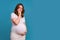 Portrait of a pregnant woman with a puzzled questioning look on a blue background