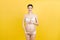 Portrait of pregnant woman in underwear wearing elastic bandage against pain in the back at yellow background with copy space.