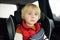 Portrait of a preschooler boy sitting in a car seat and wearing a belt. Ð¡hild bored during a family trip. Safety of children in