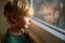 Portrait of preteen boy standing at the window. Child watching the rain outside