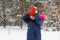 Portrait of preteen happy girl outside putting red warm hat on nature winter snowy forest background. Pretty child