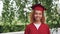 Portrait of pretty African American girl graduating student in red gown and mortarboard standing outdoors, smiling and