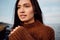 Portrait of pretty Asian brunette girl in cozy knitted sweater dreamily looking away on seaside
