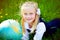 Portrait of pretty blond school girl discovering the globe on the grass outdoors