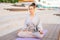 Portrait of pretty blonde serene young woman meditating on yoga mat in lotus position holding hand on knee, outside in