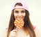 Portrait pretty cool young girl wearing a pink baseball cap with sweet caramel lollipop