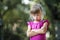 Portrait of pretty funny moody young blond child girl in pink sleeveless dress looks in camera feeling angry and unsatisfied on b