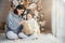 Portrait of pretty girl and beautiful female mother sit together on warm carpet, hold present box, enjoy decorated New Year tree.