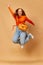 Portrait of pretty girl, student wearing bright clothes, jeans jumping and smiling on ginger studio background