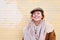 Portrait of a pretty hipster woman wearing hat outside smiling to camera. Yellow brick wall behind, daylight.