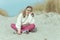 Portrait of pretty little girl sitting on white sand in dunes on Baltic sea