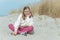 Portrait of pretty little girl sitting on white sand in dunes on Baltic sea