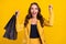 Portrait of pretty lucky cheerful wavy-haired woman holding bags rejoicing having fun  over vivid yellow color