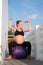 Portrait of pretty pregnant woman exercises with fitball and dumbbells outdoors