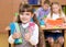 Portrait of pretty preschool girl with books in classroom showing thumb up