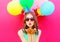 Portrait pretty woman in a birthday cap is sends an air kiss holds an air colorful balloons on pink background
