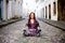 Portrait of a pretty woman with braids in her hair sitting on the sidewalk of a historic cobbled street against houses in the