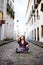 Portrait of a pretty woman with braids in her hair sitting on the sidewalk of a historic cobbled street against houses in the