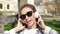 Portrait of pretty woman in sunglasses and headphones listening music, singing and dancing outdoors