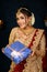 Portrait of a pretty young Indian woman dressed in traditional lehenga, gold jewellery and bangles holding gift box in hands on