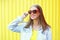 Portrait pretty young smiling woman in red sunglasses over yellow background
