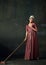 Portrait of pretty young woman in image of renaissance maid cleaning floor with mop and eating lollipop against vintage