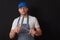 Portrait of a professional butcher in black and white apron, white t shirt and blue baseball hat. Sharpening his knives on a steel