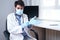 Portrait of professional confident young male doctor in medical mask and white coat, wearing gloves