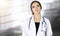 Portrait of a professional friendly woman doctor with a stethoscope, standing straight in a sunny clinic. Physician at