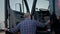 Portrait of Professional Truck Driver sits in his truck and Behind Him Parked Long Haul Semi-Truck. Close up