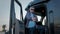 Portrait of Professional Truck Driver sits in his truck and Behind Him Parked Long Haul Semi-Truck. Close up