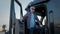 Portrait of Professional Truck Driver sits in his truck and Behind Him Parked Long Haul Semi-Truck. Close up shot