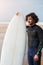 Portrait of professional young surfer standing against the ocean holding his beautiful surfboard